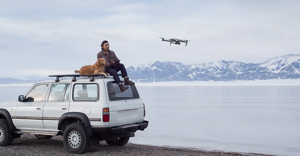 mężczyzna sterujący DJI Air 2 S siedzący na samochodzie z psem nad jeziorem