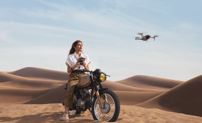 Kobieta siedząca na motocyklu na środku pustyni steruje dronem DJI Mavic Air 2